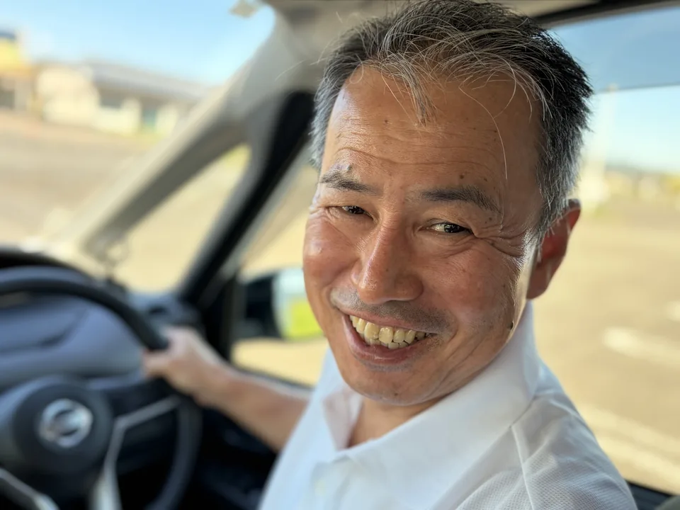 福祉タクシー いろはの運転席でハンドルを握り、笑顔で振り返る代表の川畑