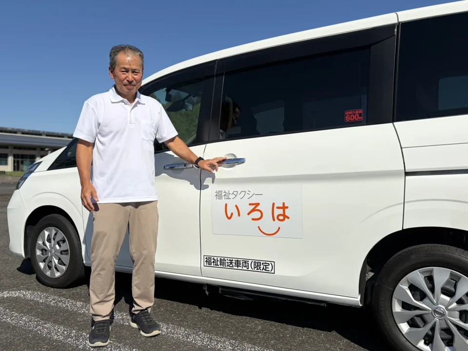 福祉タクシー いろはの車両（日産セレナ 福祉車両）の横に立つ代表の川畑